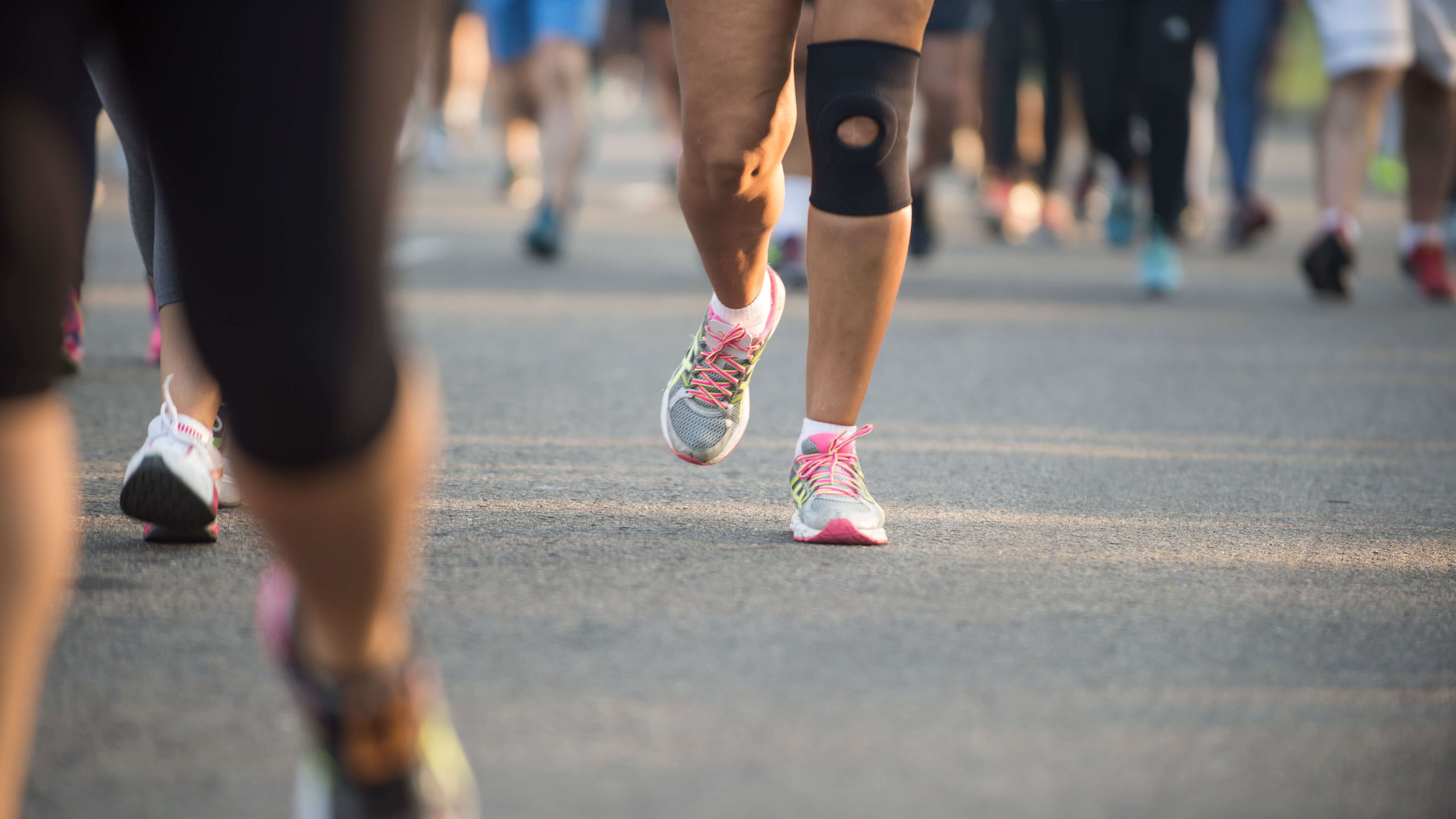 Eine Marathon-Läuferin mit Schutzbandage am Knie läuft eine asphaltierte Strasse entlang